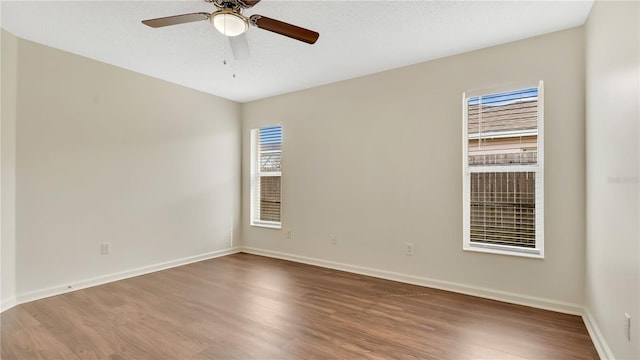 unfurnished room with a textured ceiling, wood finished floors, a ceiling fan, and baseboards