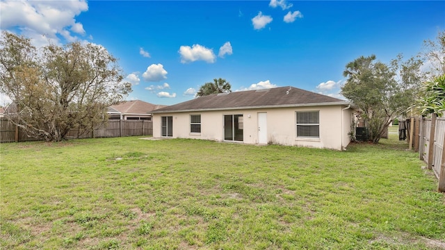 rear view of house with central air condition unit, a fenced backyard, a lawn, and stucco siding