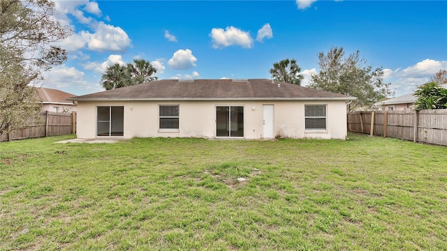 rear view of house featuring a fenced backyard, a yard, and stucco siding