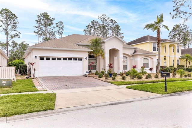 view of front of property featuring an attached garage, a front yard, decorative driveway, and stucco siding