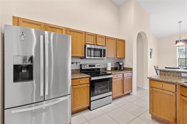 kitchen with light tile patterned floors, arched walkways, appliances with stainless steel finishes, stone counters, and pendant lighting