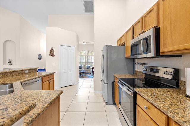 kitchen featuring light tile patterned floors, visible vents, appliances with stainless steel finishes, brown cabinets, and light stone counters