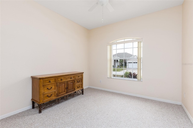 carpeted spare room featuring ceiling fan and baseboards