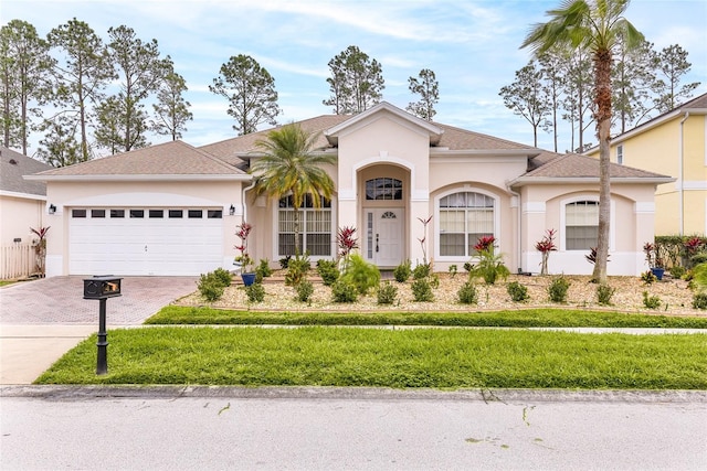 view of front of house with a garage, decorative driveway, a front lawn, and stucco siding