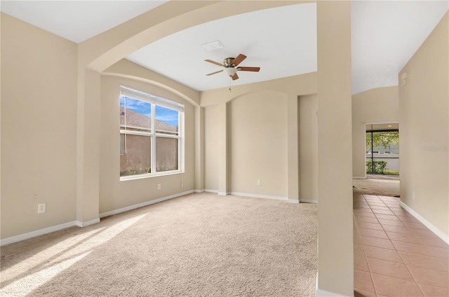 empty room featuring light tile patterned floors, baseboards, arched walkways, a ceiling fan, and light colored carpet