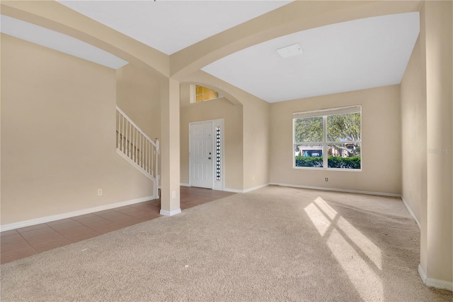 unfurnished living room with carpet, arched walkways, baseboards, and stairs