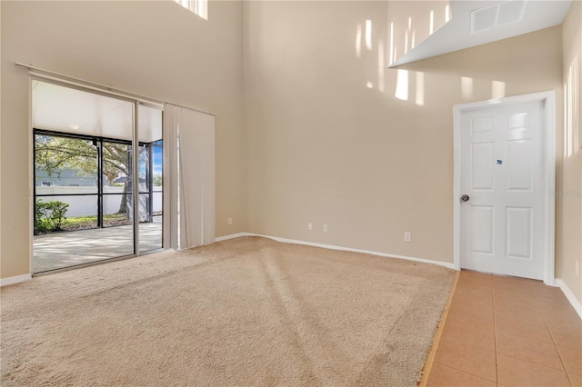 tiled spare room with carpet floors, a high ceiling, visible vents, and baseboards