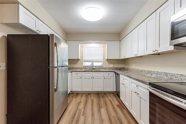 kitchen with light stone counters, a sink, white cabinets, light wood-style floors, and appliances with stainless steel finishes