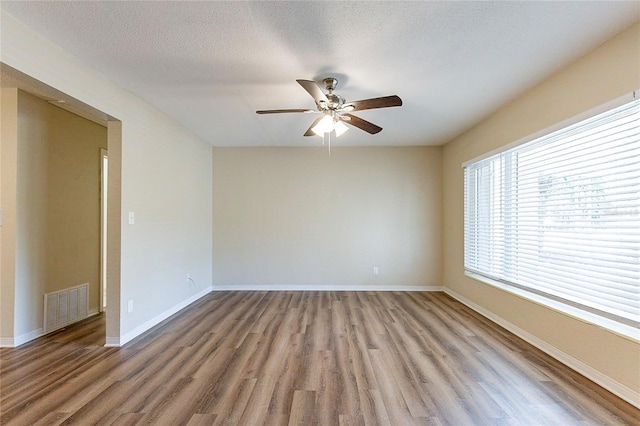 spare room with light wood finished floors, visible vents, ceiling fan, baseboards, and a textured ceiling