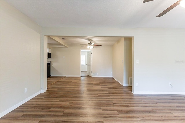 unfurnished room with a ceiling fan, wood finished floors, visible vents, baseboards, and a textured ceiling