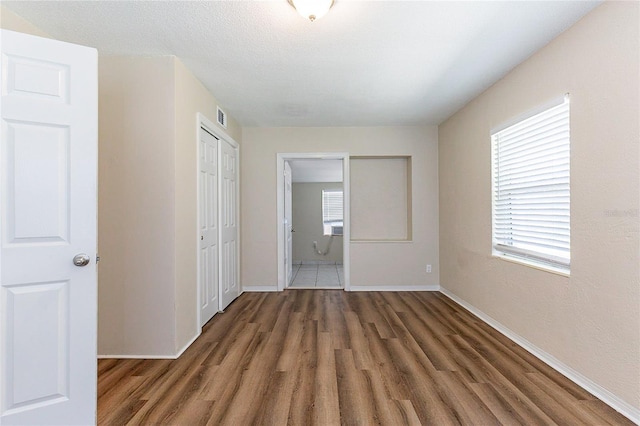 unfurnished bedroom featuring visible vents, wood finished floors, connected bathroom, a closet, and baseboards