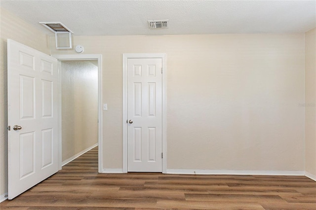 unfurnished bedroom featuring visible vents, baseboards, a textured ceiling, and wood finished floors