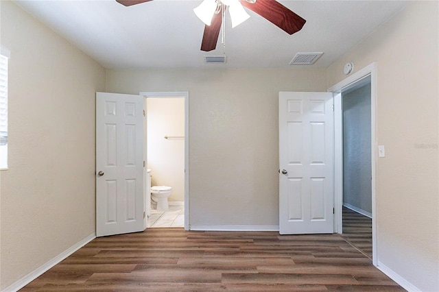 unfurnished bedroom with connected bathroom, visible vents, baseboards, and wood finished floors