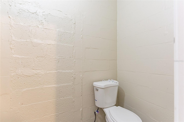 bathroom featuring toilet and concrete block wall