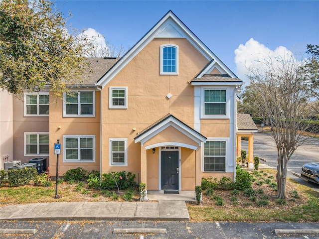 multi unit property featuring a shingled roof, cooling unit, and stucco siding