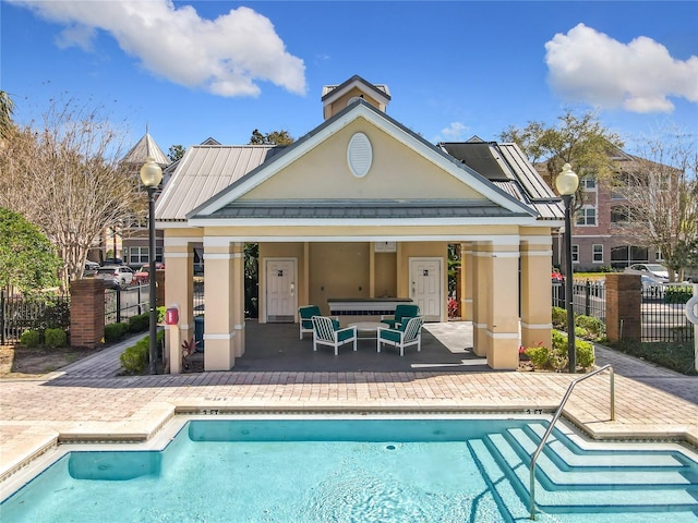 rear view of house with stucco siding, a patio area, metal roof, fence, and a community pool