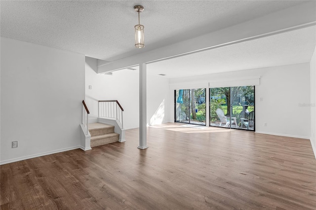 unfurnished living room with a textured ceiling, stairs, baseboards, and wood finished floors