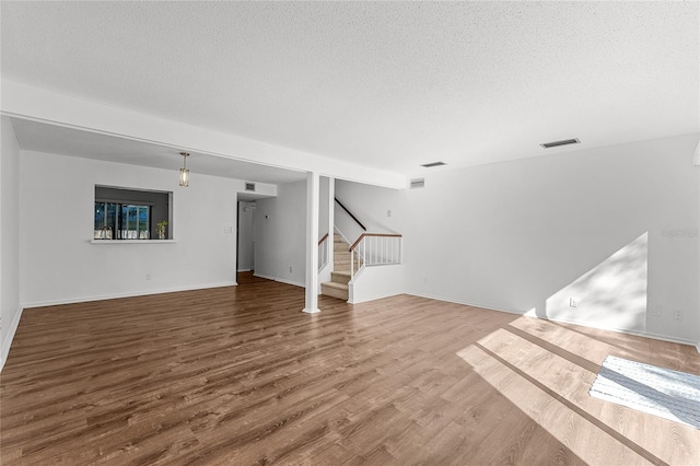 unfurnished living room with visible vents, stairway, a textured ceiling, wood finished floors, and baseboards