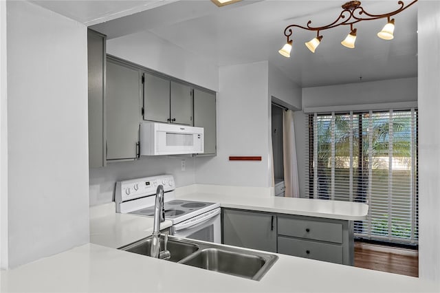 kitchen with gray cabinets, light countertops, a sink, white appliances, and a peninsula