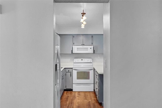 kitchen featuring pendant lighting, gray cabinets, light countertops, wood finished floors, and white appliances