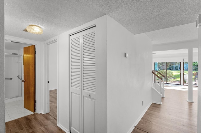 hallway featuring a textured ceiling, baseboards, and wood finished floors