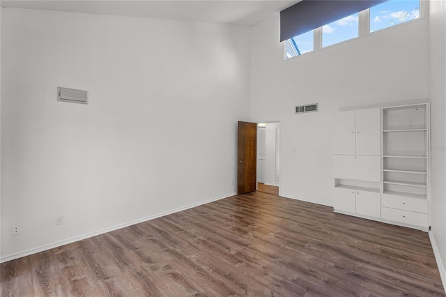 unfurnished living room with a towering ceiling, wood finished floors, visible vents, and baseboards