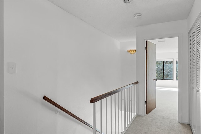 hall with an upstairs landing and light colored carpet