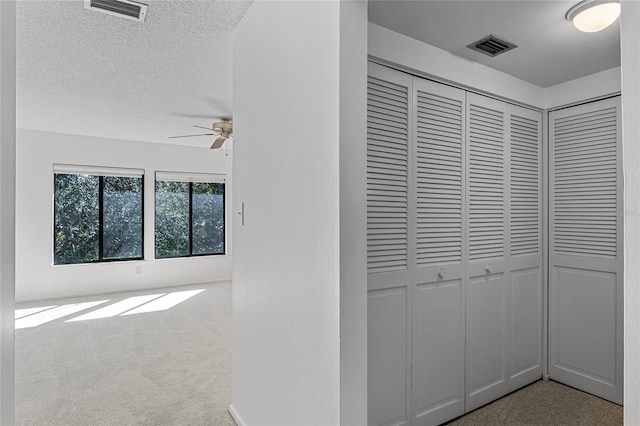 hall with a textured ceiling, carpet, and visible vents