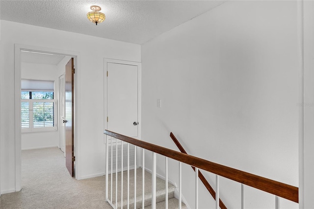 corridor with a textured ceiling, baseboards, and light colored carpet