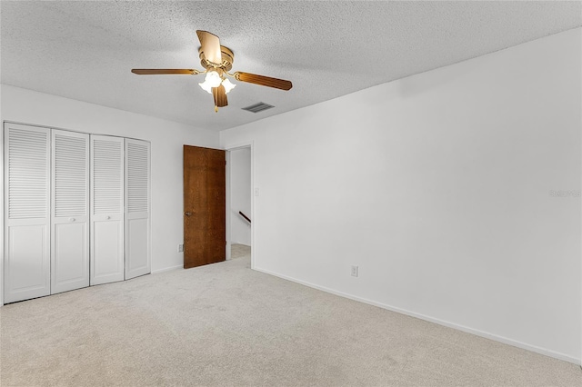 unfurnished bedroom featuring a textured ceiling, visible vents, baseboards, a closet, and carpet