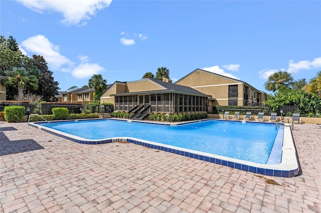 community pool with a patio area, fence, and a sunroom