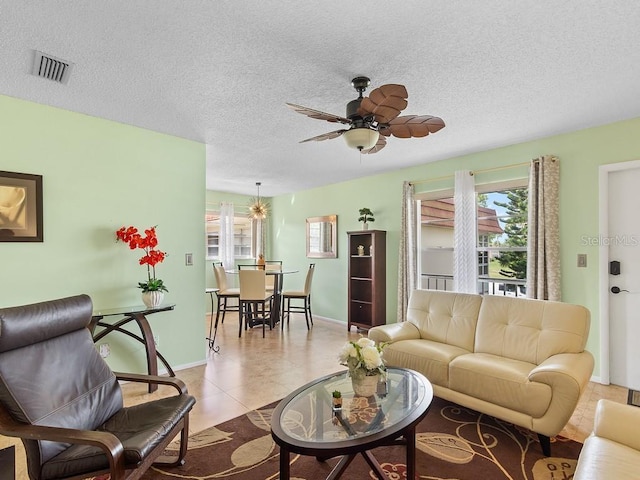 living area featuring a textured ceiling, tile patterned flooring, visible vents, baseboards, and a ceiling fan