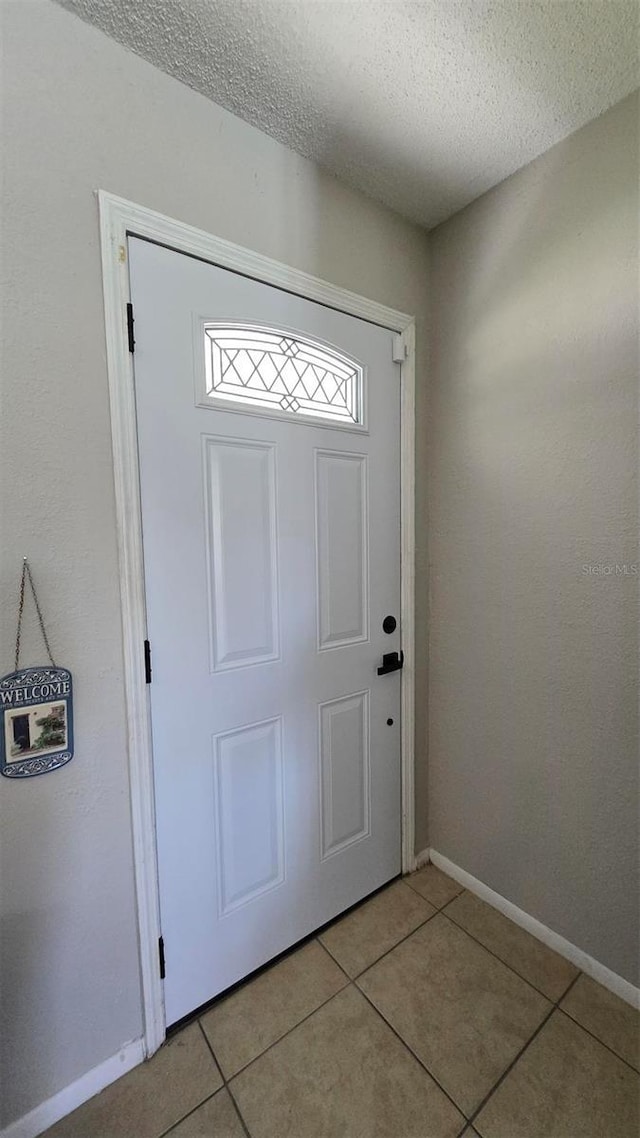 doorway with light tile patterned floors, a textured ceiling, and baseboards