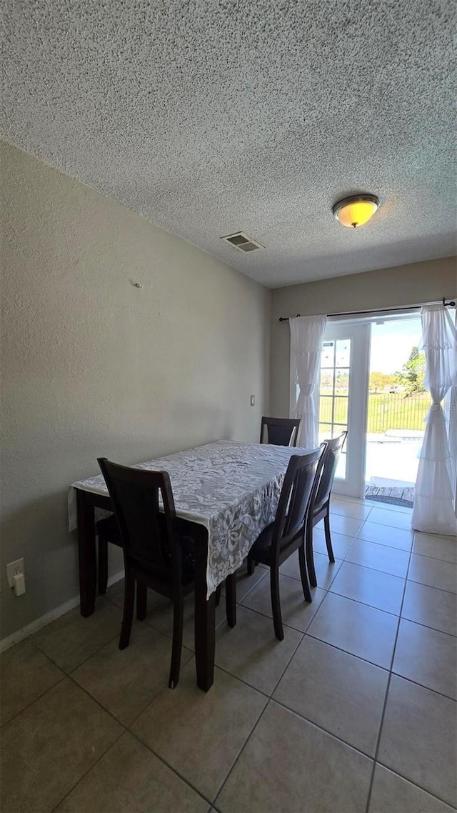 dining area with light tile patterned floors, a textured ceiling, visible vents, and baseboards