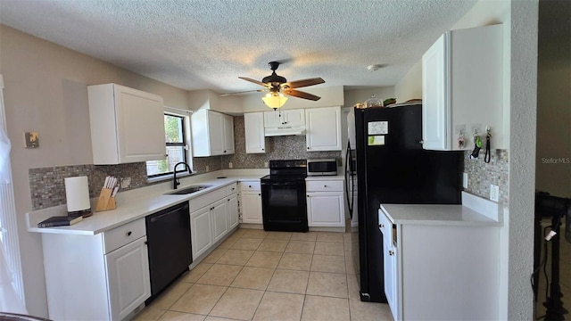 kitchen featuring light tile patterned floors, white cabinets, a sink, under cabinet range hood, and black appliances