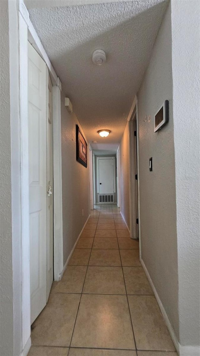 hallway featuring light tile patterned floors, visible vents, a textured wall, a textured ceiling, and baseboards