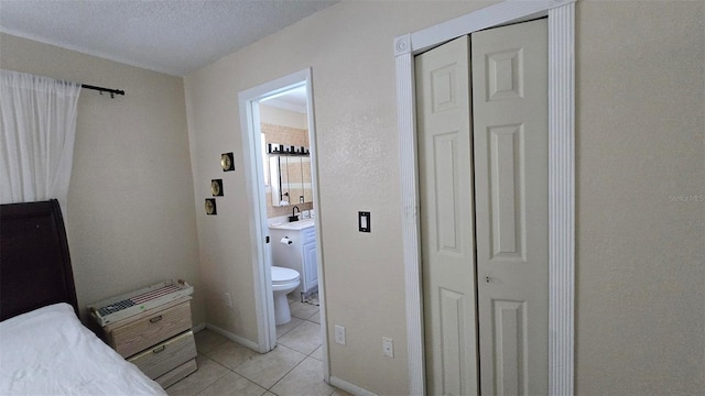 bedroom featuring light tile patterned floors, a textured ceiling, a sink, a closet, and ensuite bath