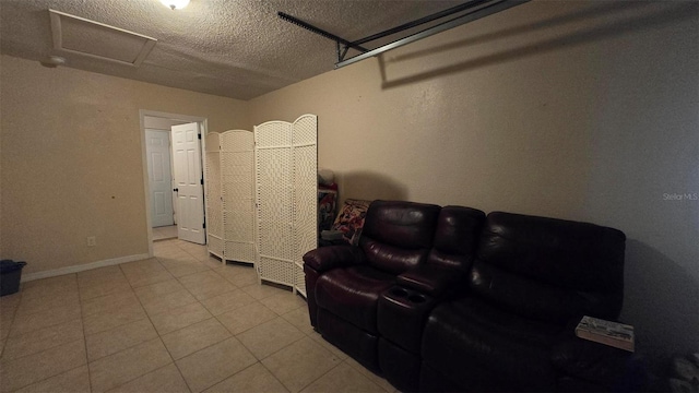 living area with a textured ceiling, tile patterned flooring, attic access, and baseboards