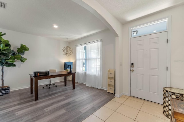 entrance foyer featuring arched walkways, a textured ceiling, visible vents, baseboards, and light wood-style floors