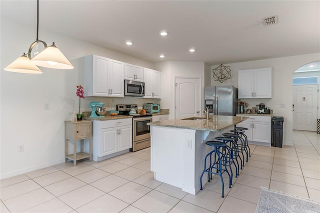 kitchen featuring arched walkways, appliances with stainless steel finishes, a kitchen bar, white cabinetry, and a sink