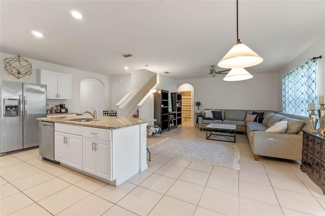 kitchen with light tile patterned floors, arched walkways, white cabinets, stainless steel appliances, and a sink