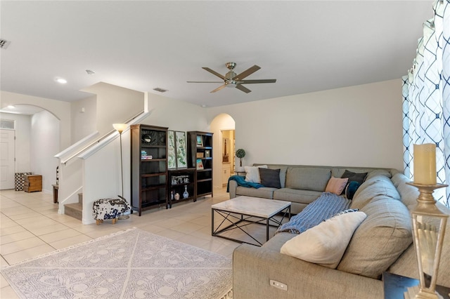 living area with light tile patterned floors, visible vents, arched walkways, a ceiling fan, and stairway