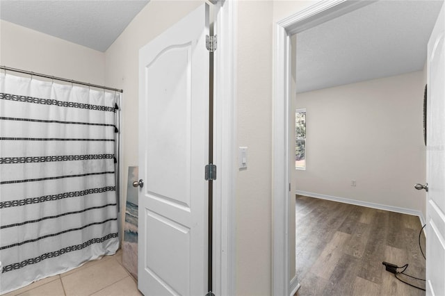 full bathroom featuring a textured ceiling, curtained shower, wood finished floors, and baseboards