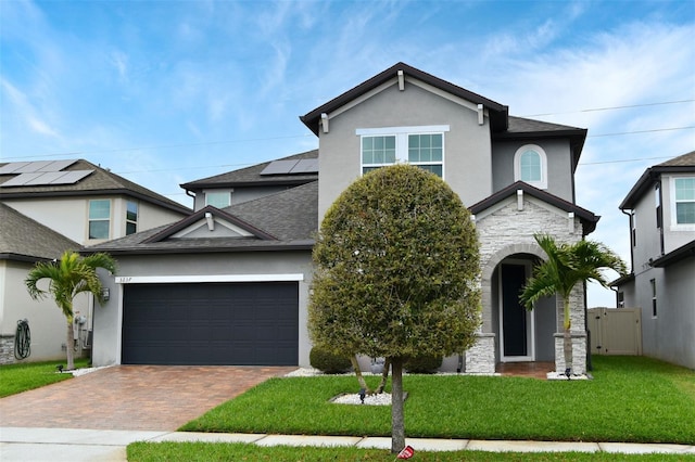 traditional-style house with an attached garage, stone siding, decorative driveway, stucco siding, and a front lawn