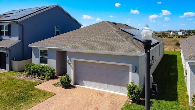 view of front of house featuring decorative driveway, roof with shingles, roof mounted solar panels, and an attached garage