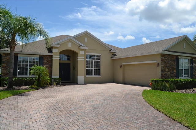 ranch-style house with a garage, stone siding, decorative driveway, and stucco siding