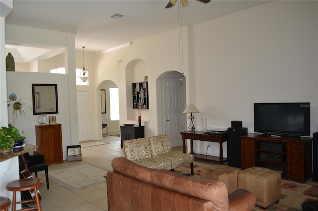 living room featuring visible vents, arched walkways, a ceiling fan, a high ceiling, and light tile patterned flooring