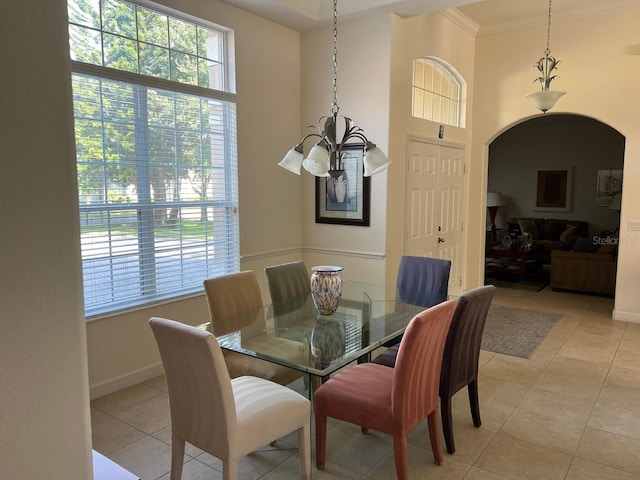 dining area with arched walkways, light tile patterned floors, a towering ceiling, ornamental molding, and baseboards