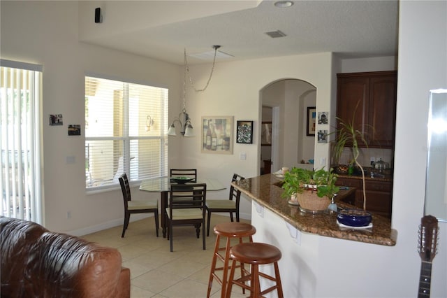 kitchen with arched walkways, visible vents, baseboards, a kitchen breakfast bar, and dark stone counters