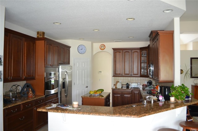 kitchen with a peninsula, appliances with stainless steel finishes, backsplash, and a breakfast bar area